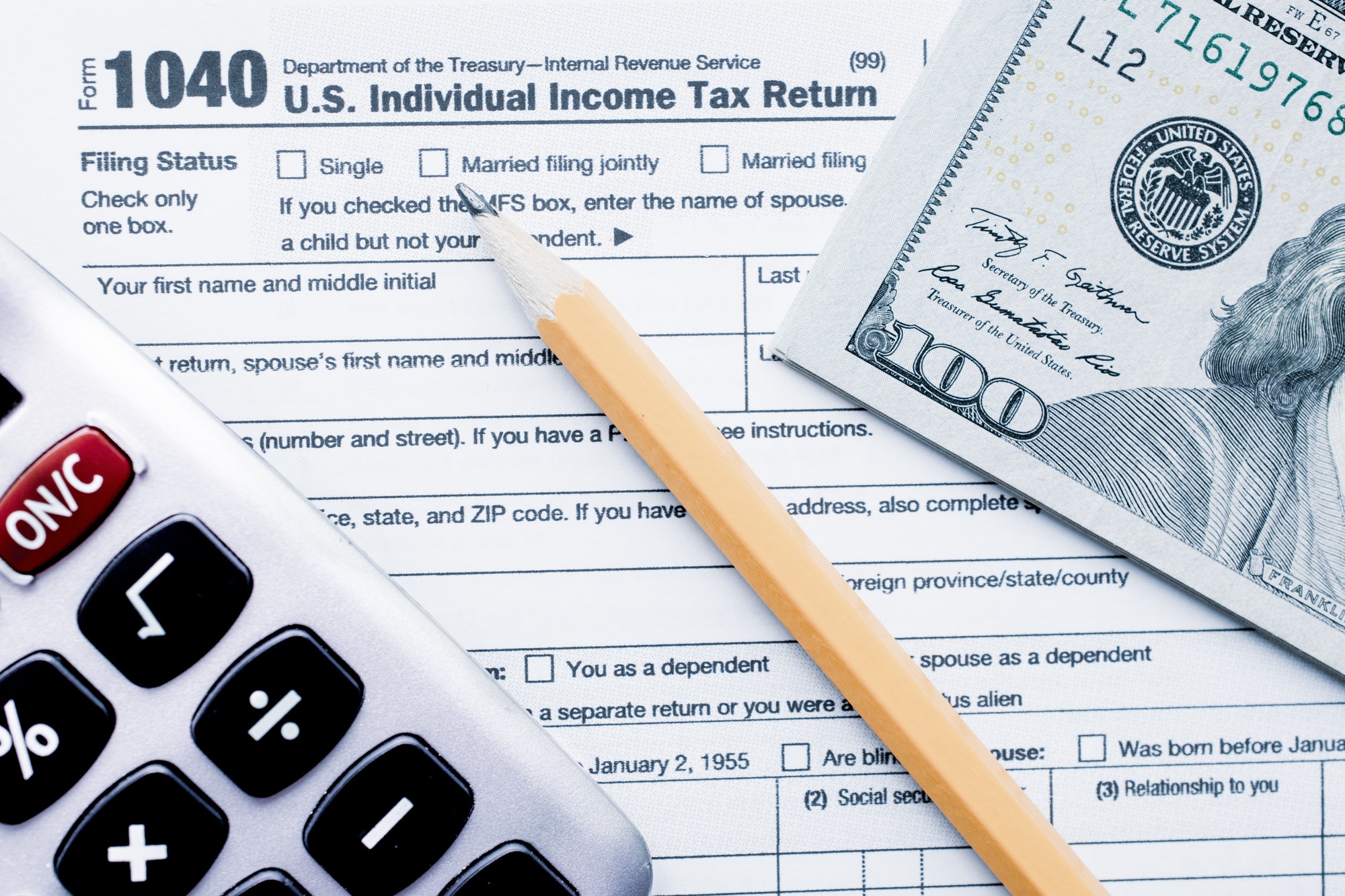U.S. Individual Income Tax Return with a calcultator, cash money $100 dollar bills with a pencil
